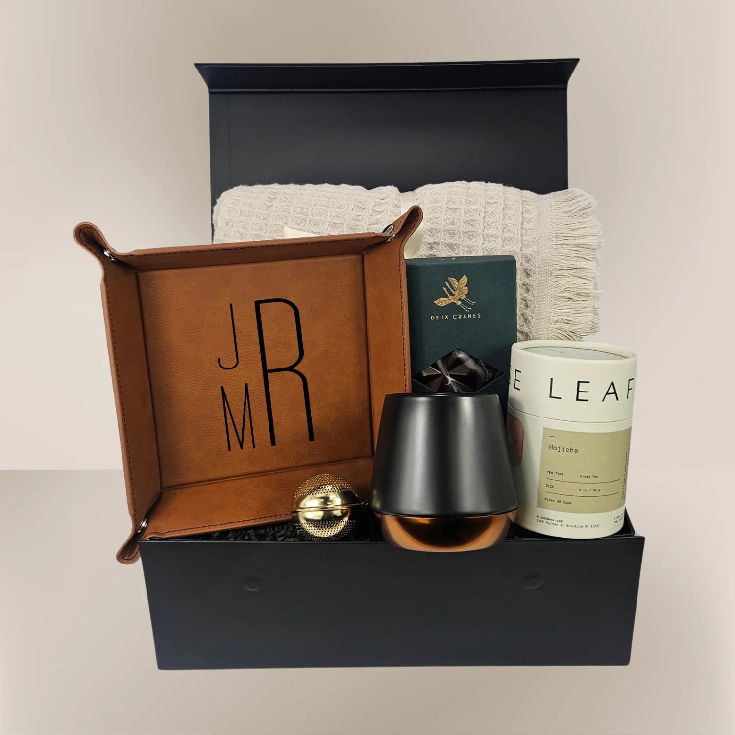 Luxury gift box with personalized monogrammed leather tray, woven throw, candle, tea, and chocolate